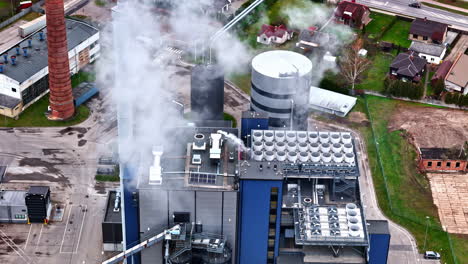 a large industrial power plant with steam rising from cooling towers and chimneys , aerial view