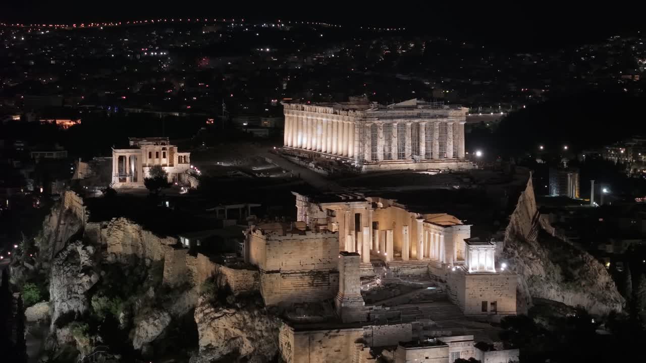 Night drone orbit capturing the illuminated Acropolis and Parthenon during Easter, with bright fireworks lighting the Athenian sky in a stunning festive display