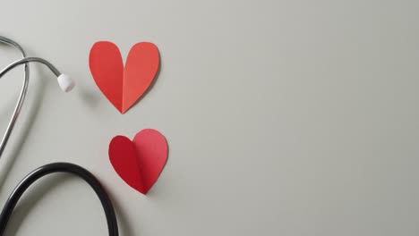 video of stethoscope with two red paper hearts on grey background with copy space