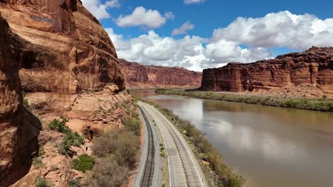 aerial view, flying over highway next to colorado river, red cliffs, railroad tracks, blue sky with white fluffy clouds, potash road, moab utah, lower colorado river scenic byway