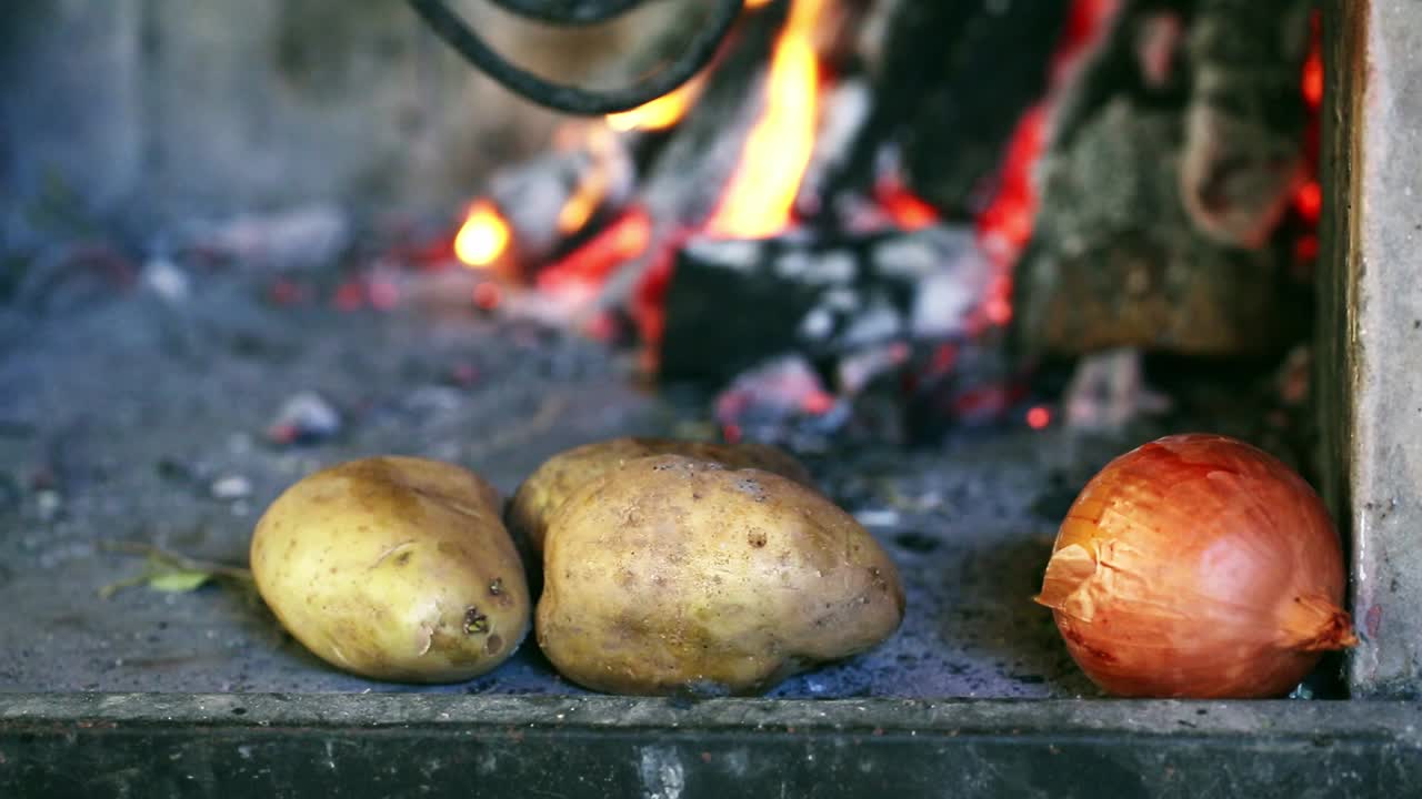papas y cebolla cerca del fuego antes de ser cocinadas en una parrilla