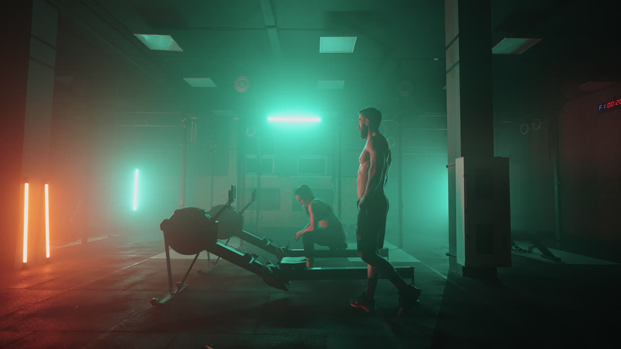 sala de gimnasia hombre y mujer están entrenando con aparatos de entrenamiento en un salón oscuro deportivo y saludable