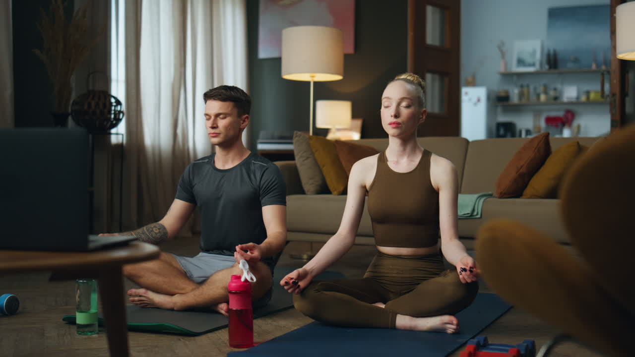 una pareja sentada en la postura del loto en casa practicando yoga. una mujer meditando con un hombre.