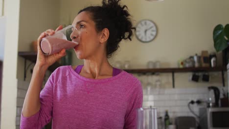 mixed race woman drinking fruit juice in the kitchen at home