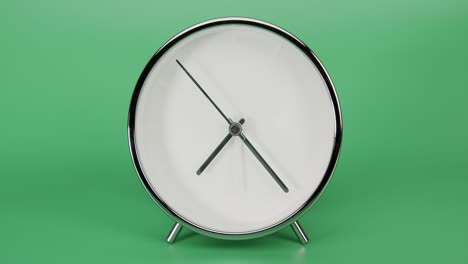 silver alarm clock isolated on green background, time starts walking at 7 o'clock.