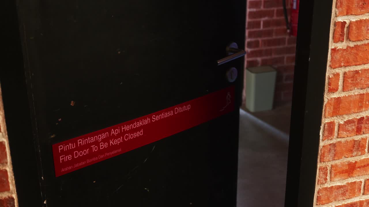 Asian man opening black fire retardant door at brick house