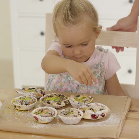 close up on girl sprinkling toppings on muffins