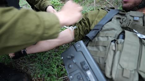 idf israeli soldier emergency medical assistance or first aid at battle field - applies a tourniquet on arm and injects needle