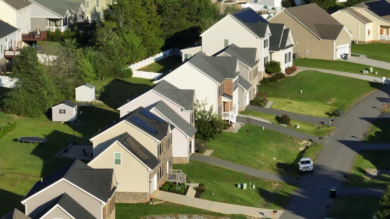 Row of modern two-story houses with solar panel in roof and green front yards. Sunset time in late summer day. American suburb neighborhood with middle class homes. Aerial zoom shot