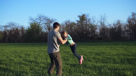 un joven padre con una hija se divierte en el campo abierto. un hombre lanza a una chica en el aire, la cosquillea, divirtiéndose juntos. primavera