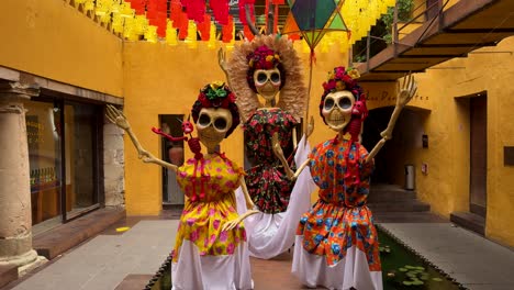 Vibrant-calaveras,-adorned-with-a-riot-of-vivid-flowers,-stand-gracefully-in-a-lively-Mexican-courtyard