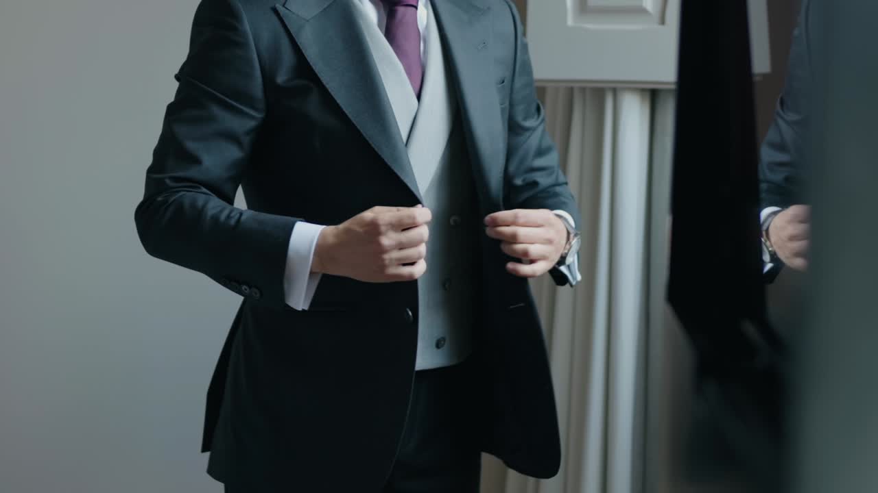Groom in elegant suit adjusting jacket indoors before wedding ceremony