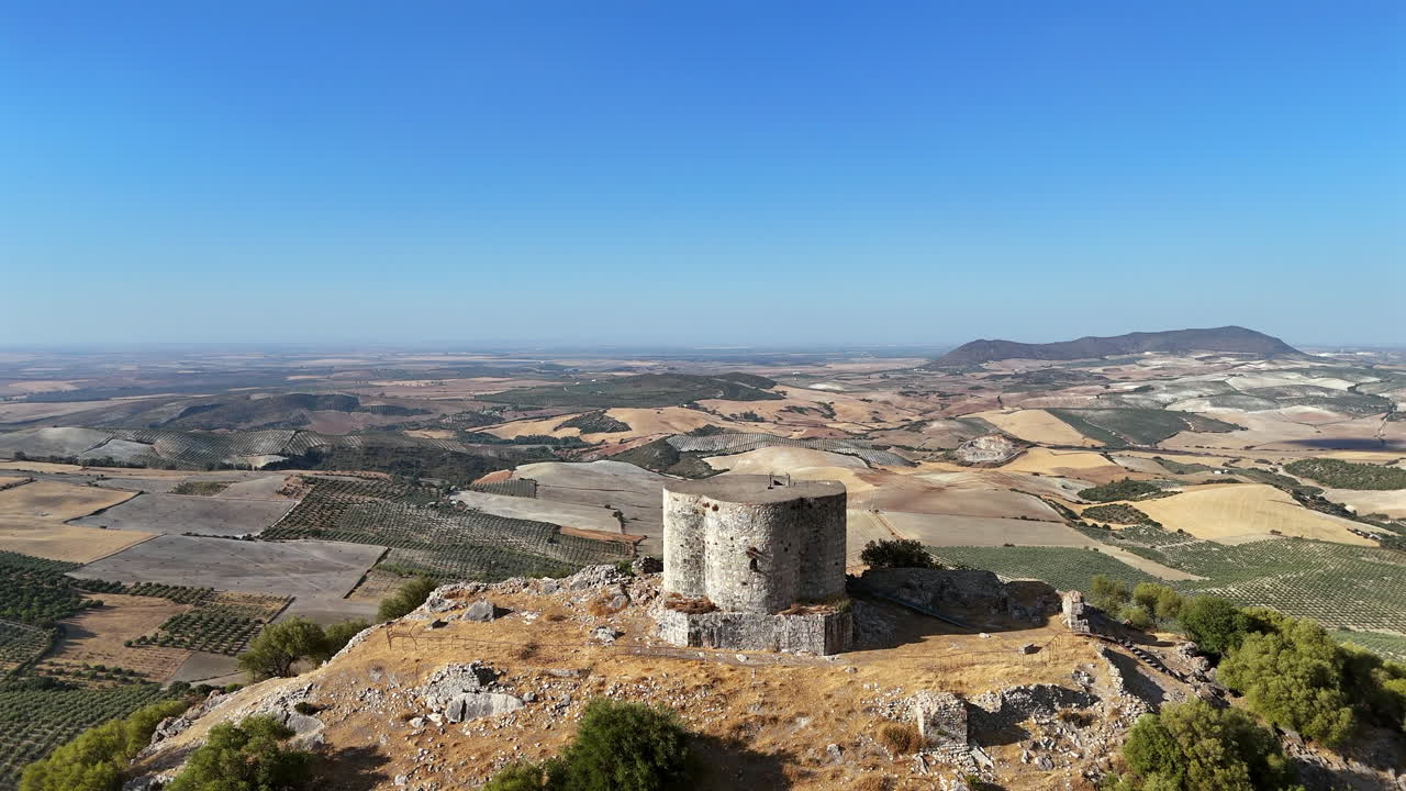 Aerial drone footage orbiting the ancient Cote Castle on a hill surrounded by farmland and valleys in Andalusia, southern Spain