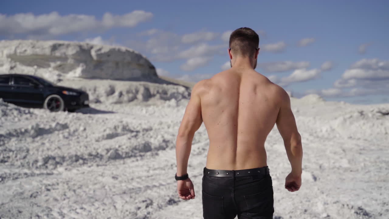 Athlete in bright sunny day on white canyon. Backside view of sporty man in nature. Shirtless bodybuilder walks in the mountains to the black car. Slow motion.