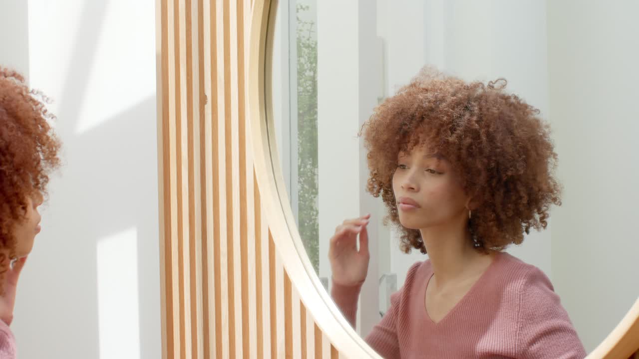 Donna afroamericana motivata dalla luce del giorno che sistema la sua acconciatura riccia allo specchio