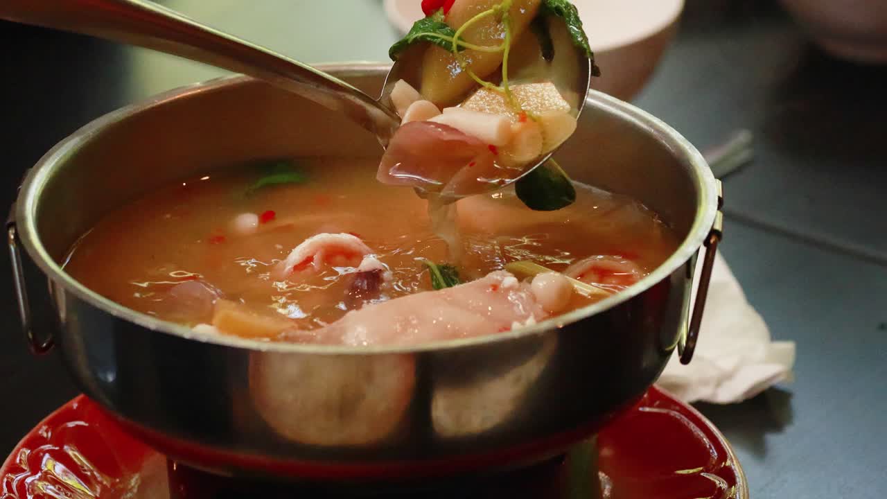 A steaming pot of Tom Yum soup with seafood ingredients being stirred in a vibrant Thai setting