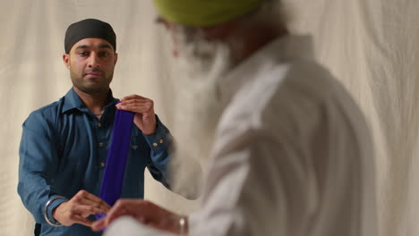 fotografía de estudio de dos hombres sikh doblando tela para turbante contra un fondo plano