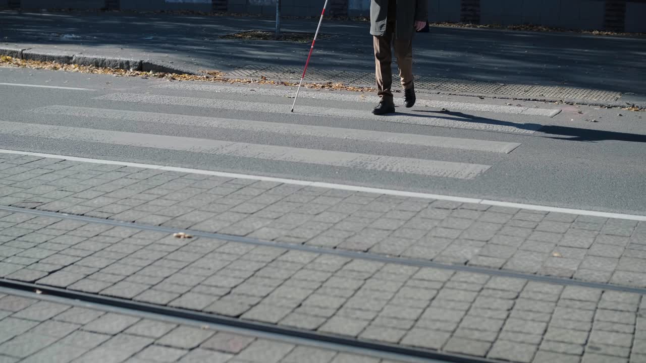 Synshemmet mann krysser veien med stokken sin ved hjelp av taktile ledelinjer for synshemmede i byen.
