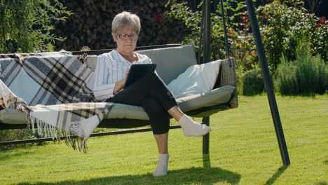 portrait of senior woman using a digital tablet. sitting in a garden swing in the backyard of a house