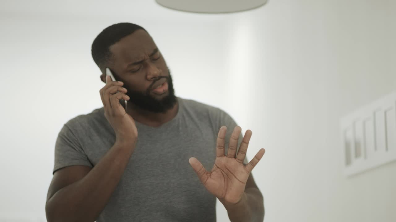 Serious black man talking phone at home kitchen. Young guy talking smartphone