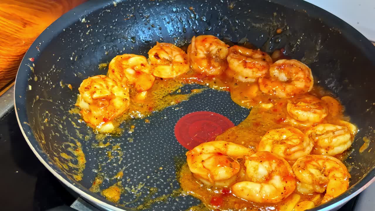 Træspatel øser kogte rejer med sauce fra en non-stick stegepande. Nærbillede.