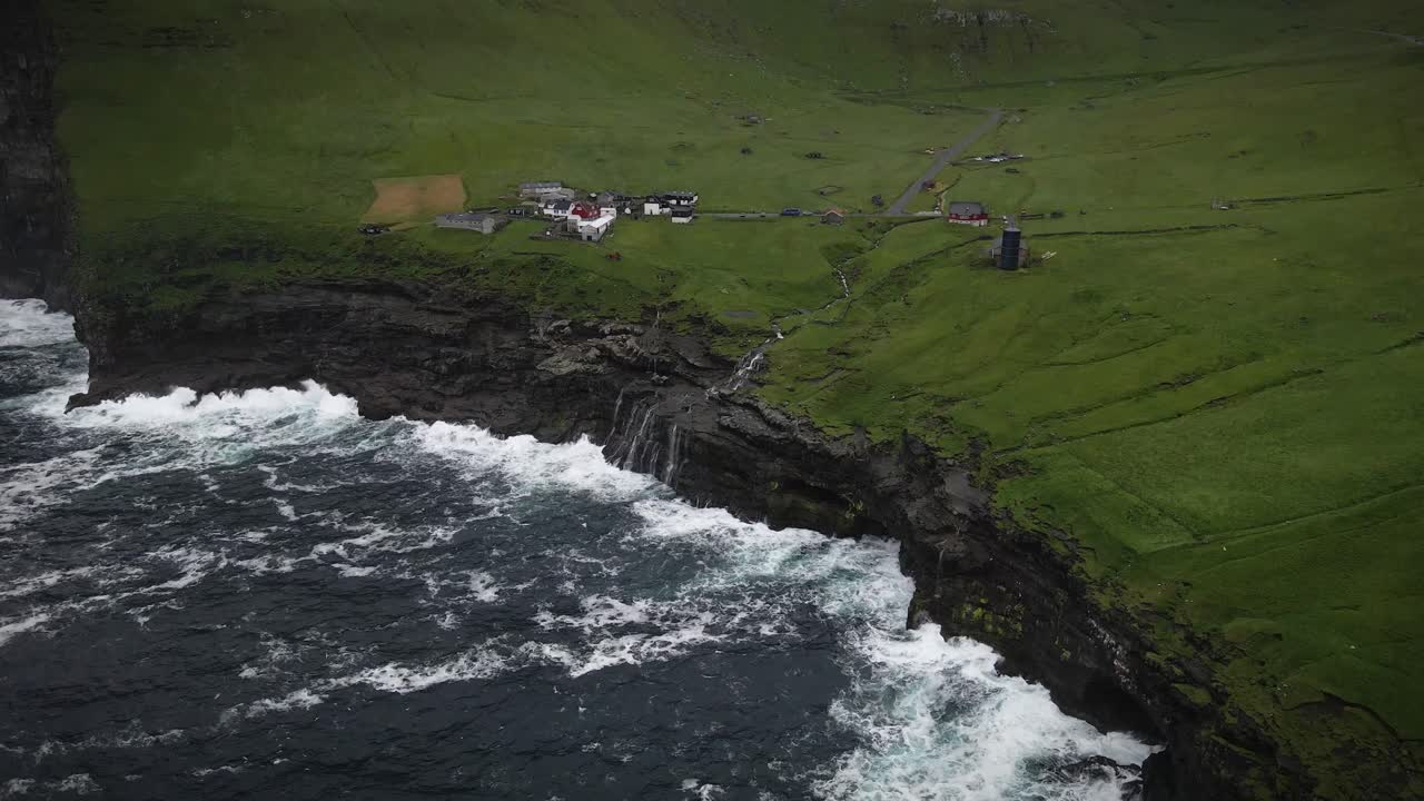 el faro de kallur en la dramática costa rocosa de la isla de kalsoy en el archipiélago de las feroe, con poderosas olas chocando contra los acantilados y la hierba verde que cubre el paisaje, cámara lenta aérea