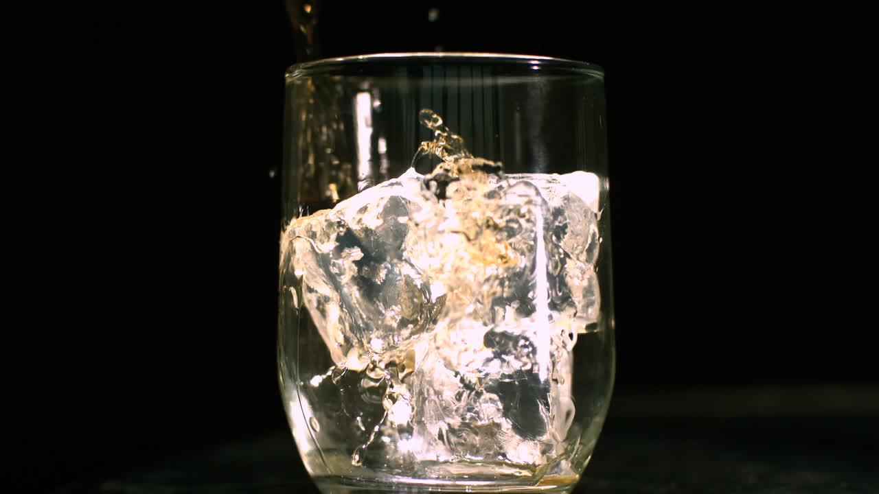whisky siendo vertido en un vaso con cubos de hielo
