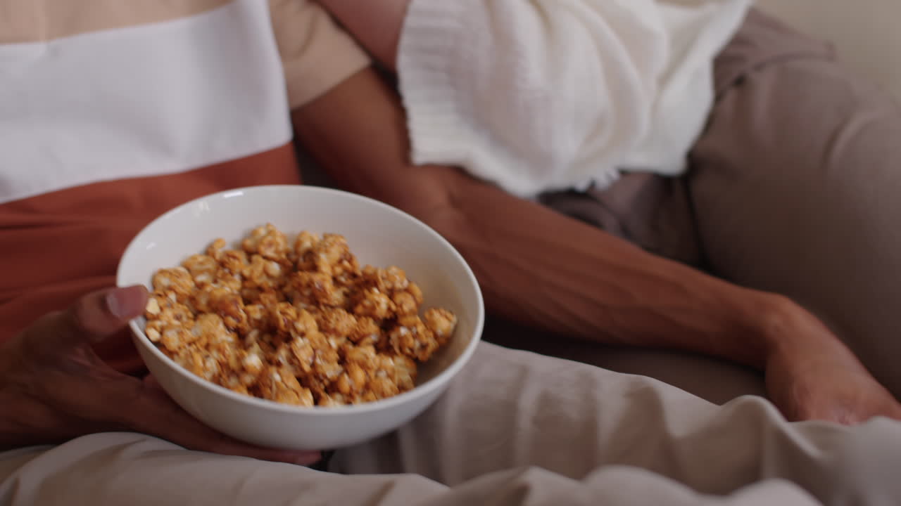 Young Spouses Feeding Each Other with Popcorn on Sofa