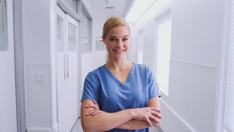 Portrait-Of-Smiling-Female-Doctor-Wearing-Scrubs-In-Hospital-Corridor