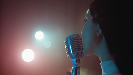 close-up side view of a singer in a white gown with beaded fringe, performing with a vintage microphone. soft, glowing lights create an intimate atmosphere