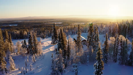 aerial view across glowing sunrise snow covered wild rural cabins surrounded by scandinavian woodland