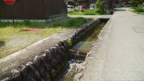 narrow waterway with clean flowing water beside empty road in shirakawago