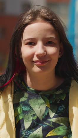 female teenager sits on swing in big city. pretty girl closes eyes fantasizing and looks into camera smiling sweetly closeup on blurred background