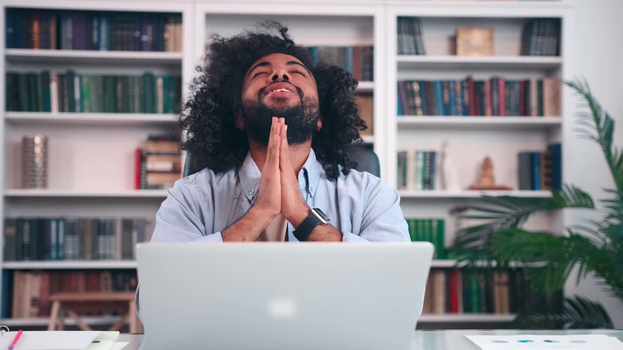 Attractive arabian man freelancer praying sits with laptop at office table