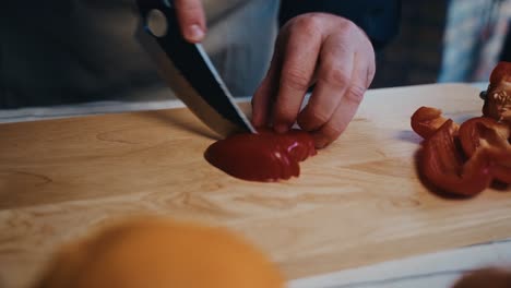 una persona cortando un pimienta de campana roja en una tabla de corte de madera con enfoque en las manos