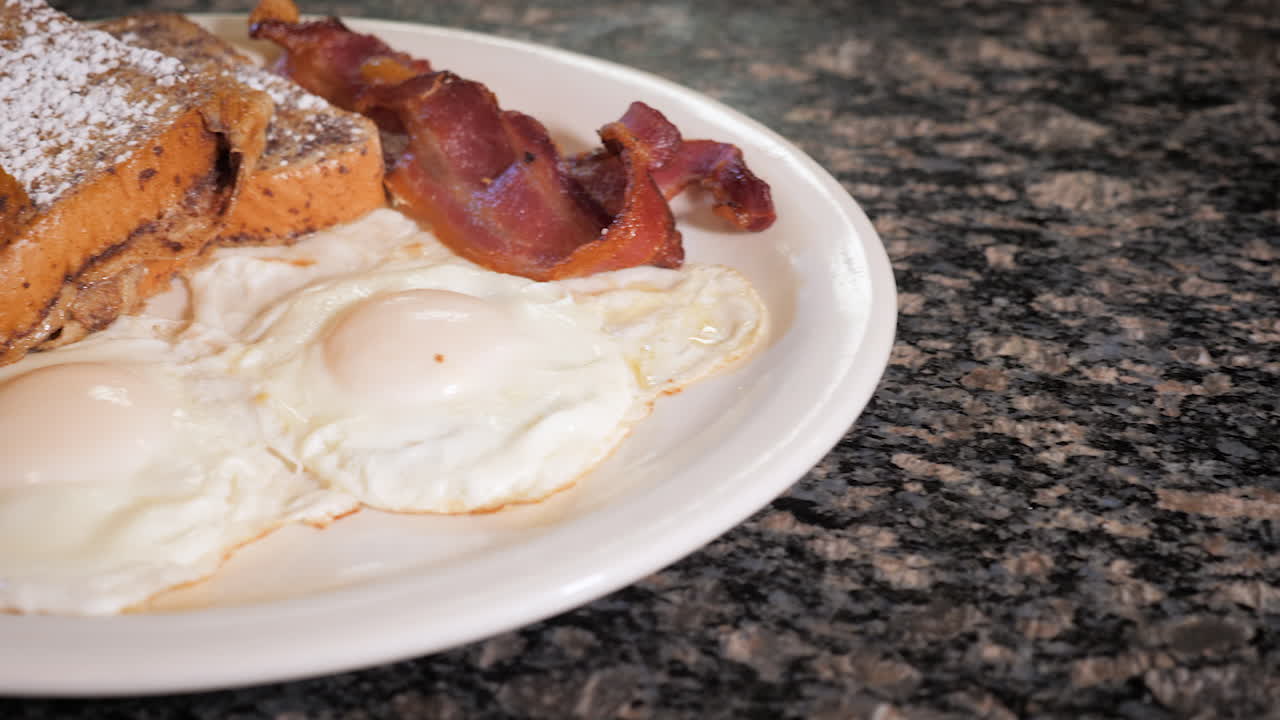 Diner breakfast on white plate, French toast fried eggs and bacon -- slider HD