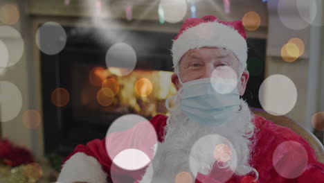 animation of covid 19 cells over santa claus in face mask and fairy lights