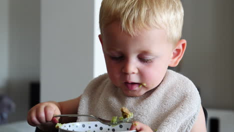 close up of cute little blond boy eating baby food with spoon