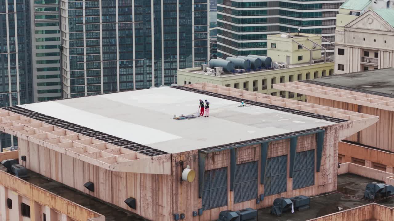 Two workers sweep, clean high rooftop showing labor routine, Metro Manila