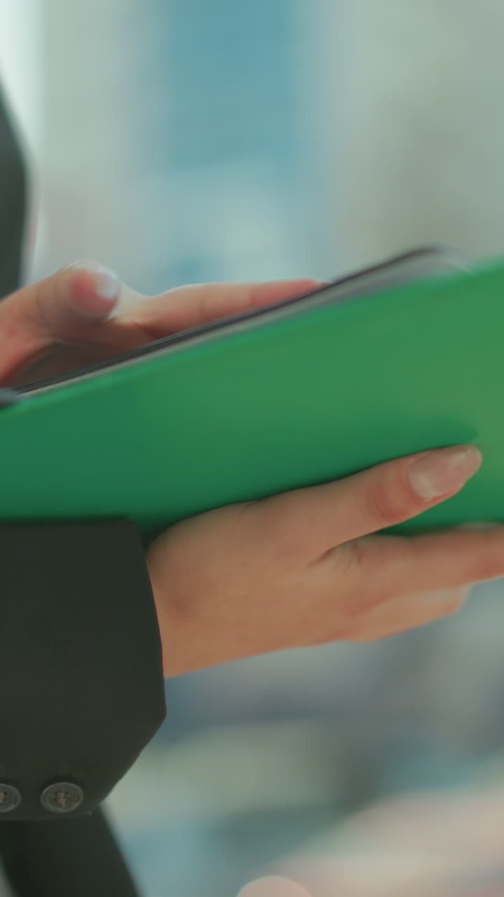 Close up of woman in formal black blazer walking outdoors cross checking file in hand with urban background featuring blurred parked cars, sunlight, and buildings during professional activity