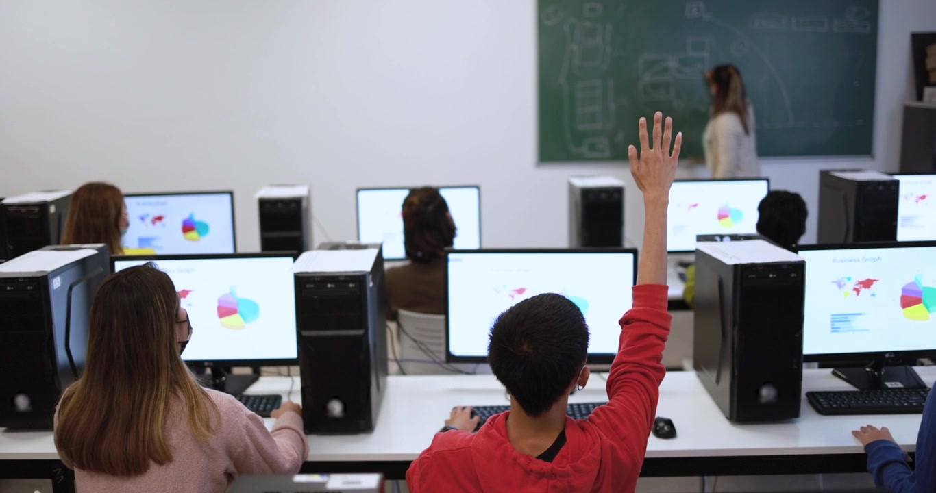 Studenti in laboratorio informatico che alzano le mani durante la lezione