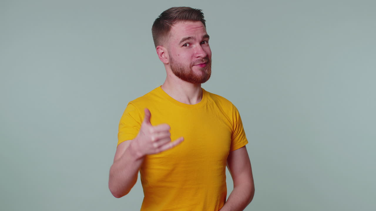 un hombre alegre en camiseta mirando a la cámara haciendo un gesto telefónico como decir hola me llamas