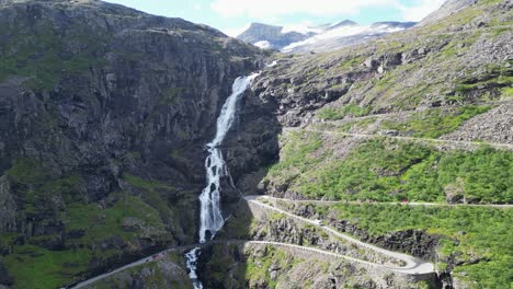 trollstigen mountain road in norway - cars driving touristic route along scenic waterfall and hairpin turns - aerial circling