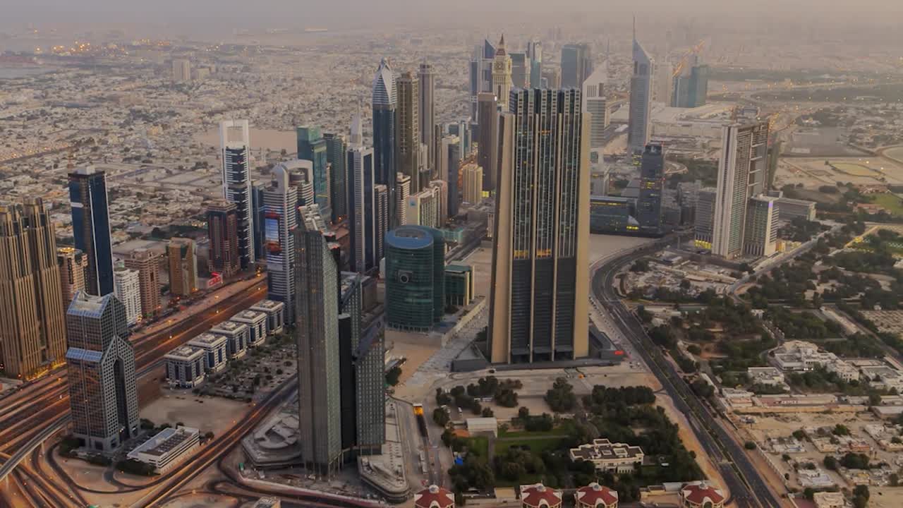 Filmato aereo in time-lapse del moderno paesaggio urbano di Dubai, caratterizzato da grattacieli ed edifici multipiano densamente raggruppati con eleganti facciate in vetro. Strade e autostrade si snodano attraverso il paesaggio urbano.