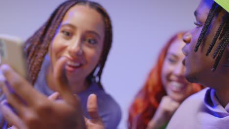 close up studio shot of young gen z friends sitting on sofa sharing social media post on mobile phones 10