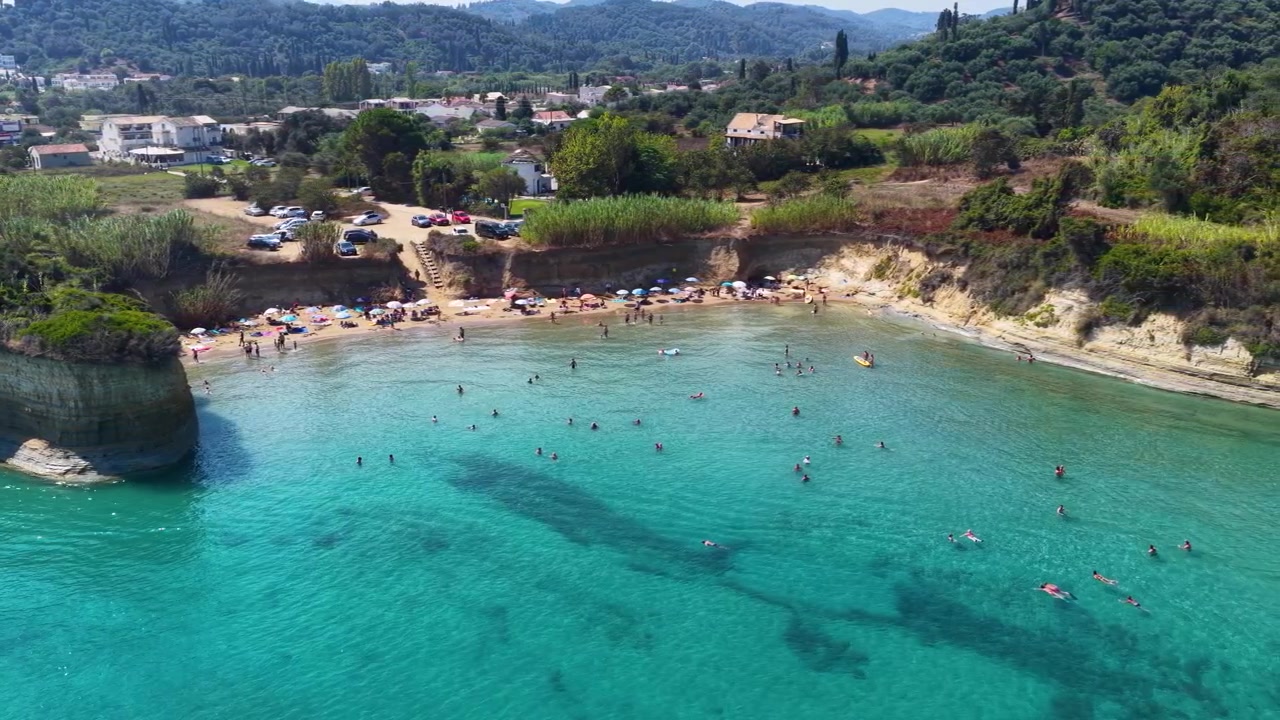 Aerial panorama of Apotripiti beach cove with turquoise sea, sandstone cliffs, tourists swimming and sandy coastline in Sidari, Corfu island, Greece, summer day view.