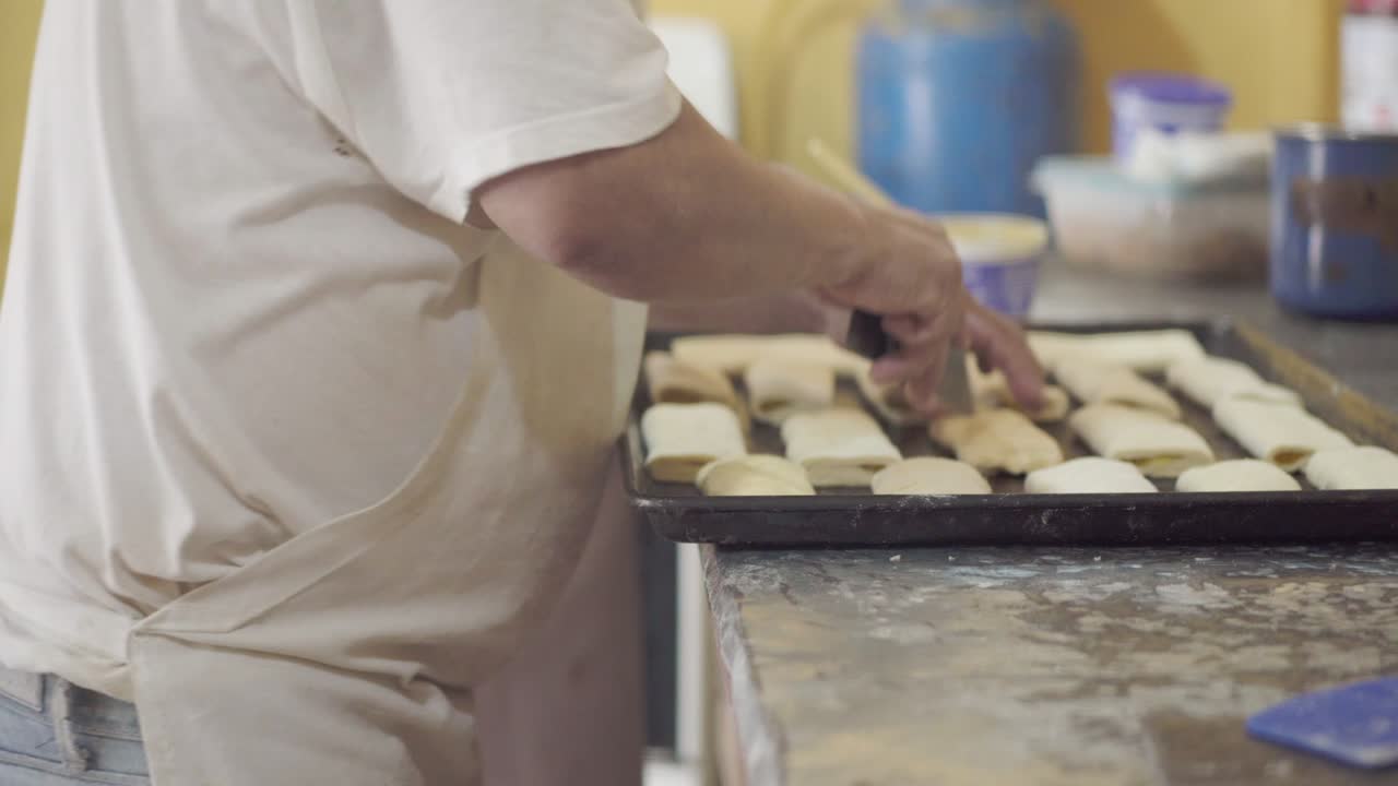 A pastry chef cuts small slits in the top of dough on a baking sheet, preparing it for baking