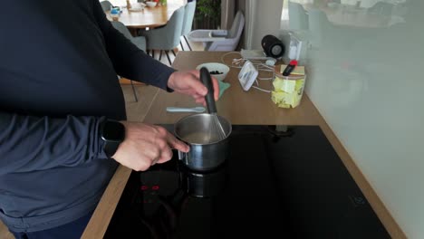 Shot-of-a-man-stirring-porridge-in-an-aluminum-pot-with-a-whisk-on-the-electric-stove-in-a-home-kitchen