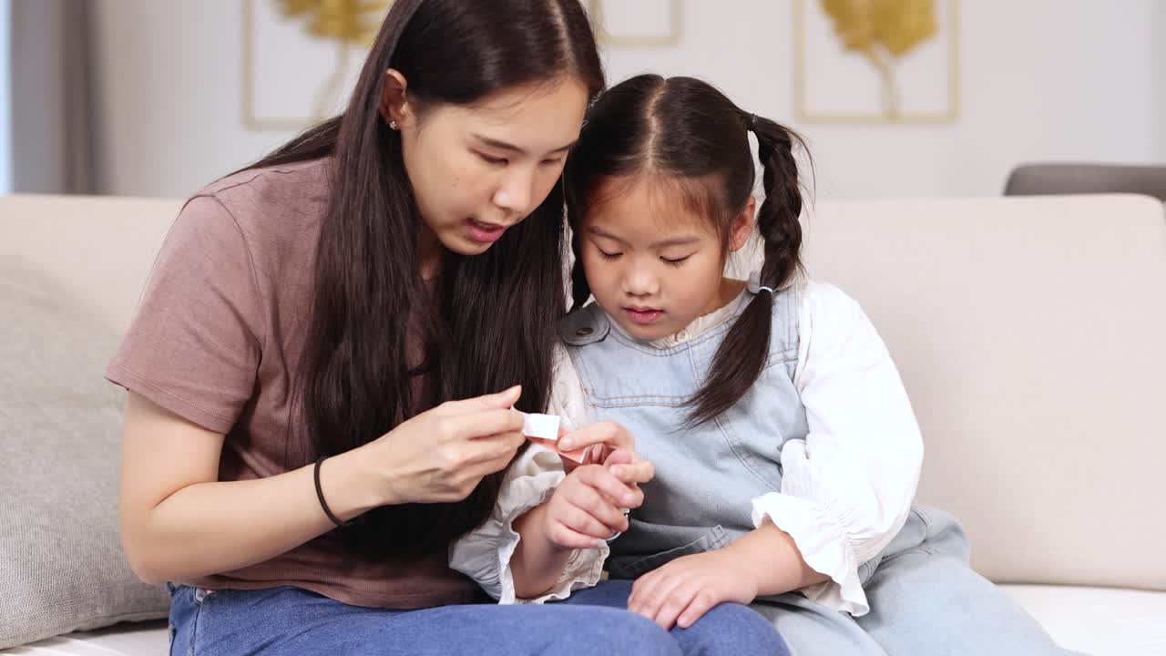 A mother helps her daughter apply a band-aid in a cozy living room setting with soft lighting