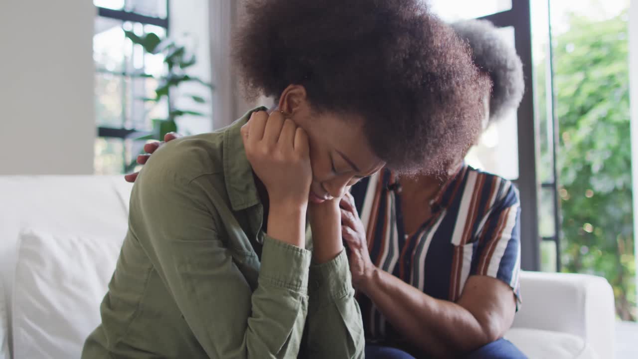 Worried african american senior mother comforting sad, crying adult daughter at home, slow motion